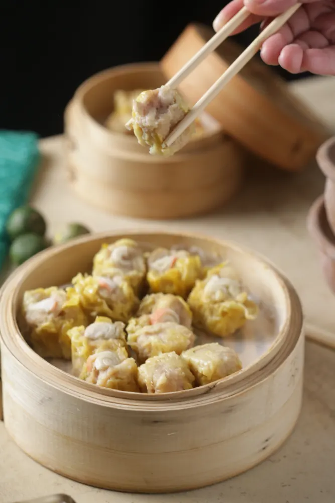 Siomai picked up with chopsticks over a bamboo steamer
